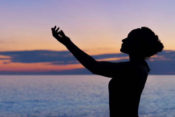 A silhouette of a woman meditating on a beach.