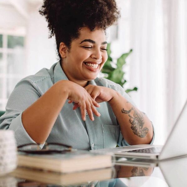 A young, plus-sized woman smiling while using a laptop.